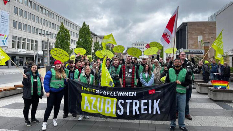 Eine große Gruppe junger Demonstrierender mit grünen Westen, gelben Fahnen und Schildern sowie einem Banner auf dem Tarifrebellinnen und Azubi Streik steht am bundesweiten Jugendaktionstag in der Tarifrunde Telekom 2024