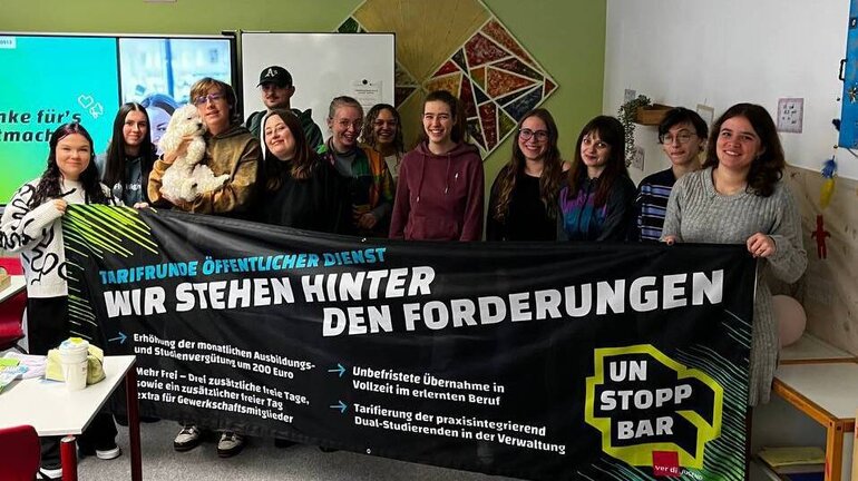 eine Gruppe an Jugendlichen hält ein Banner, auf dem die Forderungen für die Tarifrunde öffentlicher Dienst stehen.