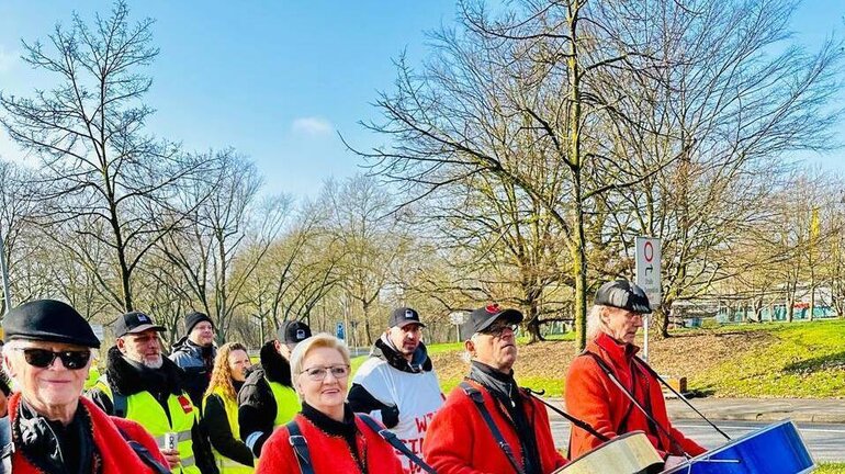 Streikende Männer und Frauen laufen mit Trommeln im Streikzug.