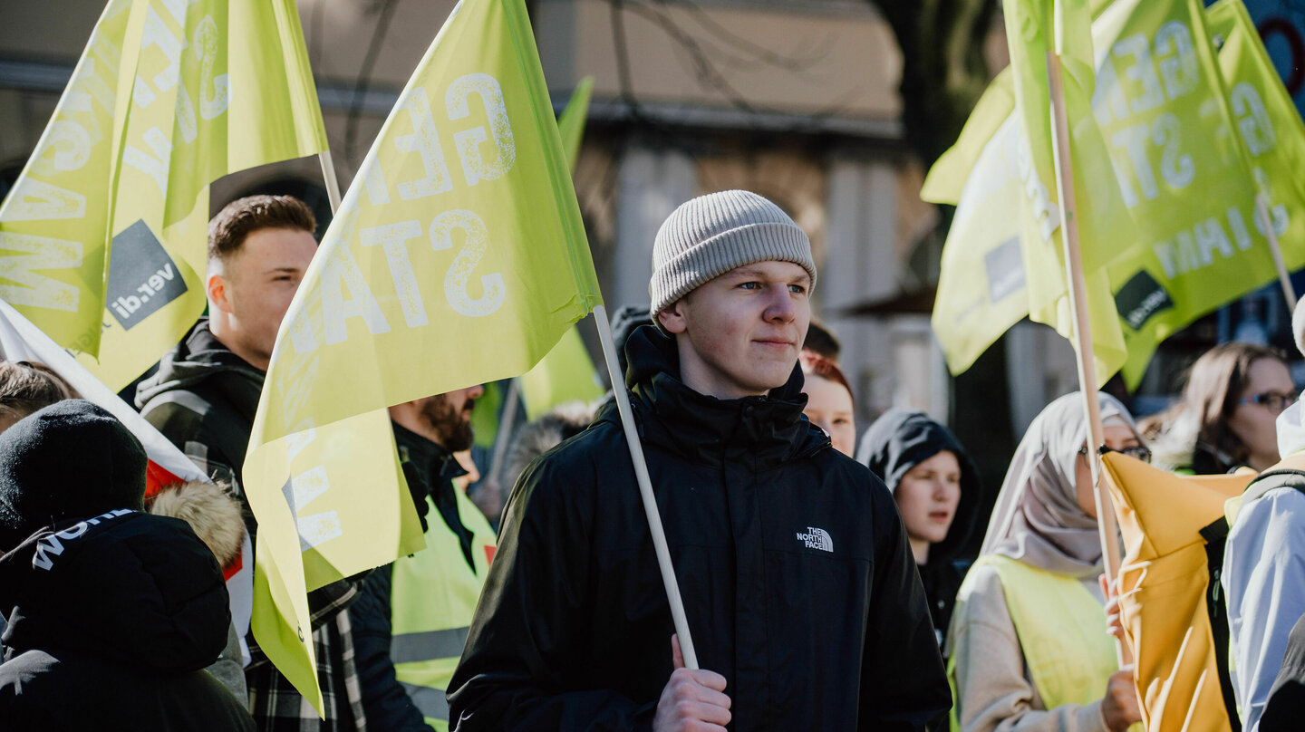 Junge Person hält Fahne und verfolgt lächelnd die Kundgebung beim Jugendstreiktag der Tarifrunde öffentlicher Dienst Bund und Kommunen in Gelsenkirchen 2023